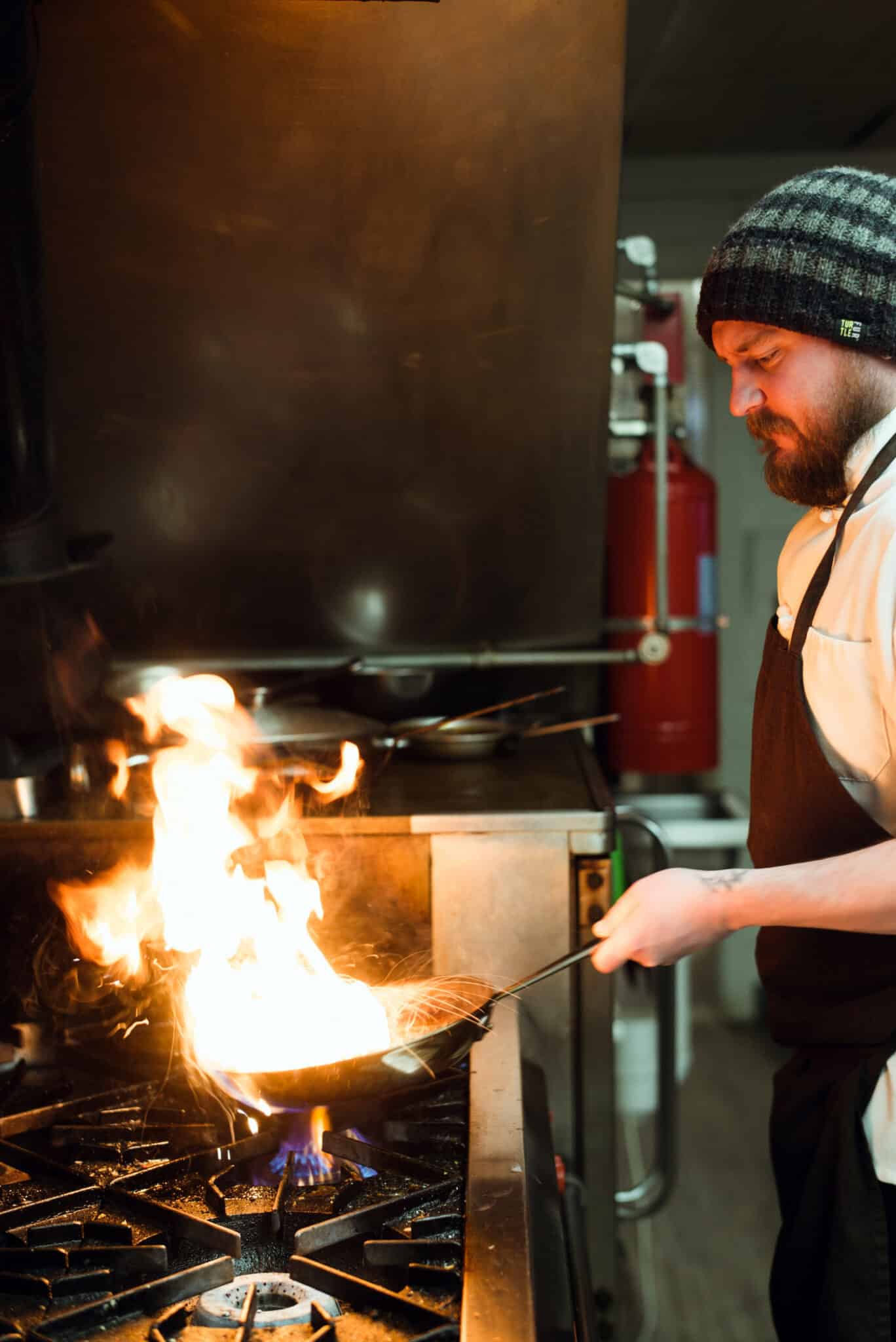 Chef Ross Moskwa tossing items in a wok with fire shooting off the top