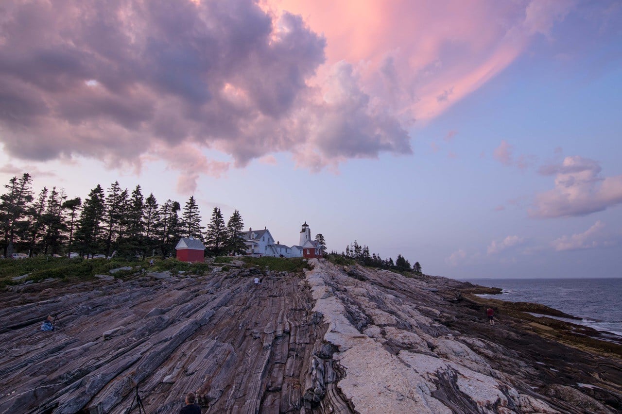 View of the Pemaquid Lighthouse looking up to it from the rocky outcropping with clouds above reflecting pink sunset rays.