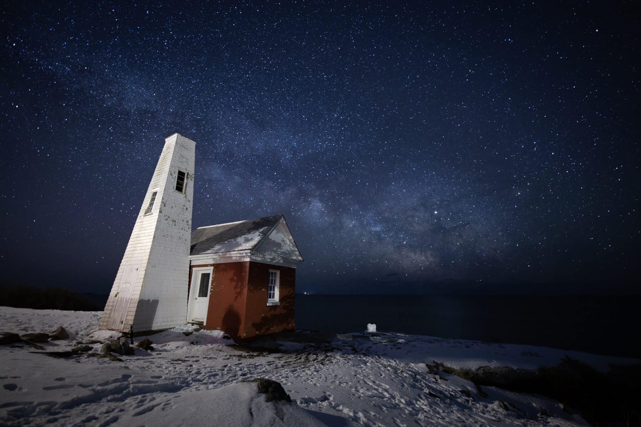Bell tower in white with red brick building sitting in front of the dark sky filled with the milky way and stars 