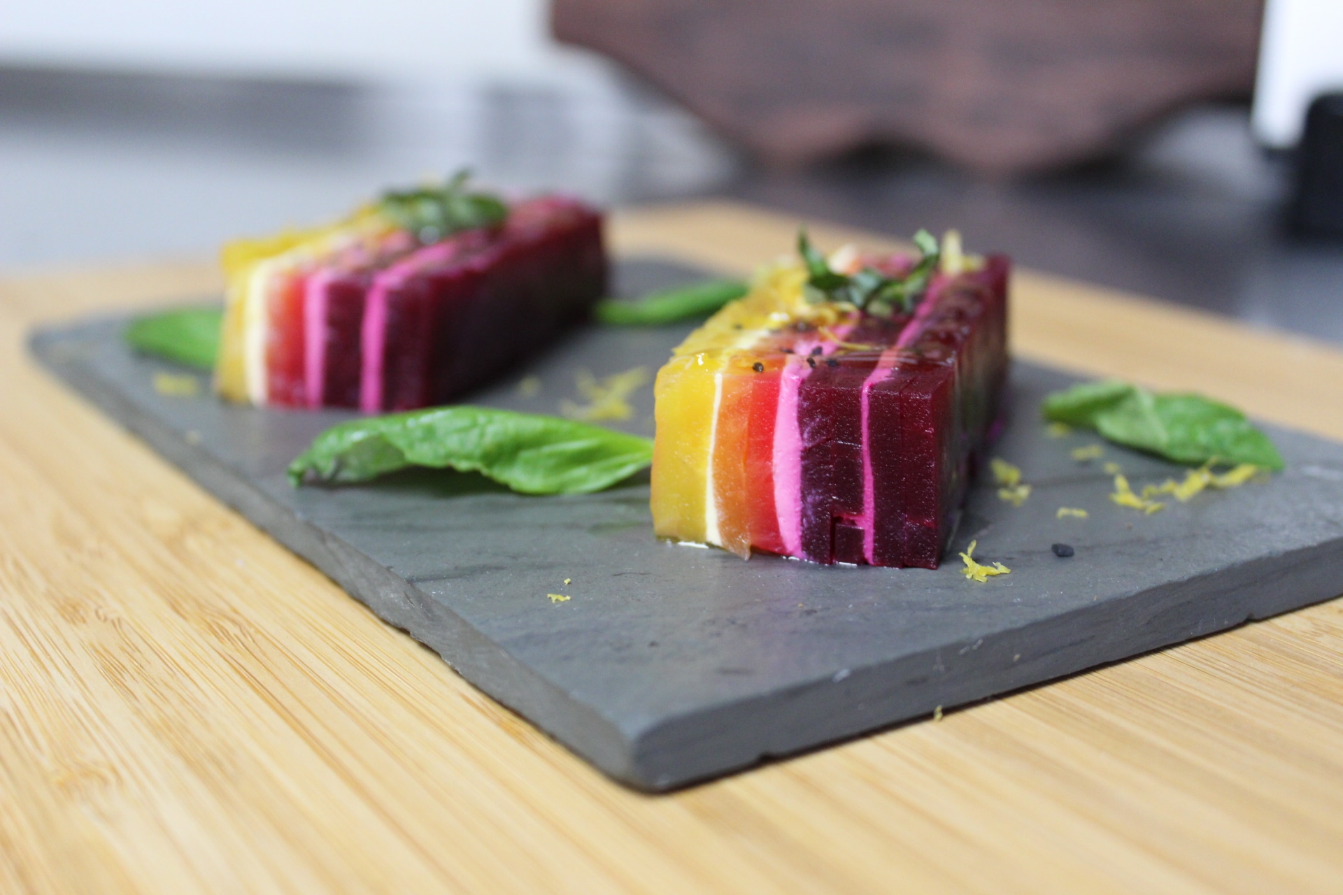 slices of colorful beets stacked in a terrine and plated on a piece of slate with greens
 