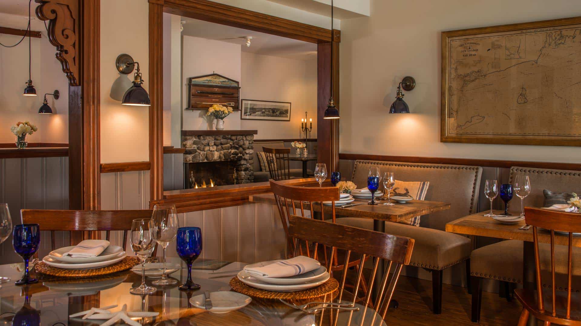 Dining room with wooden tables, wooden chairs, upholstered benches, placesettings, and fireplace in the background