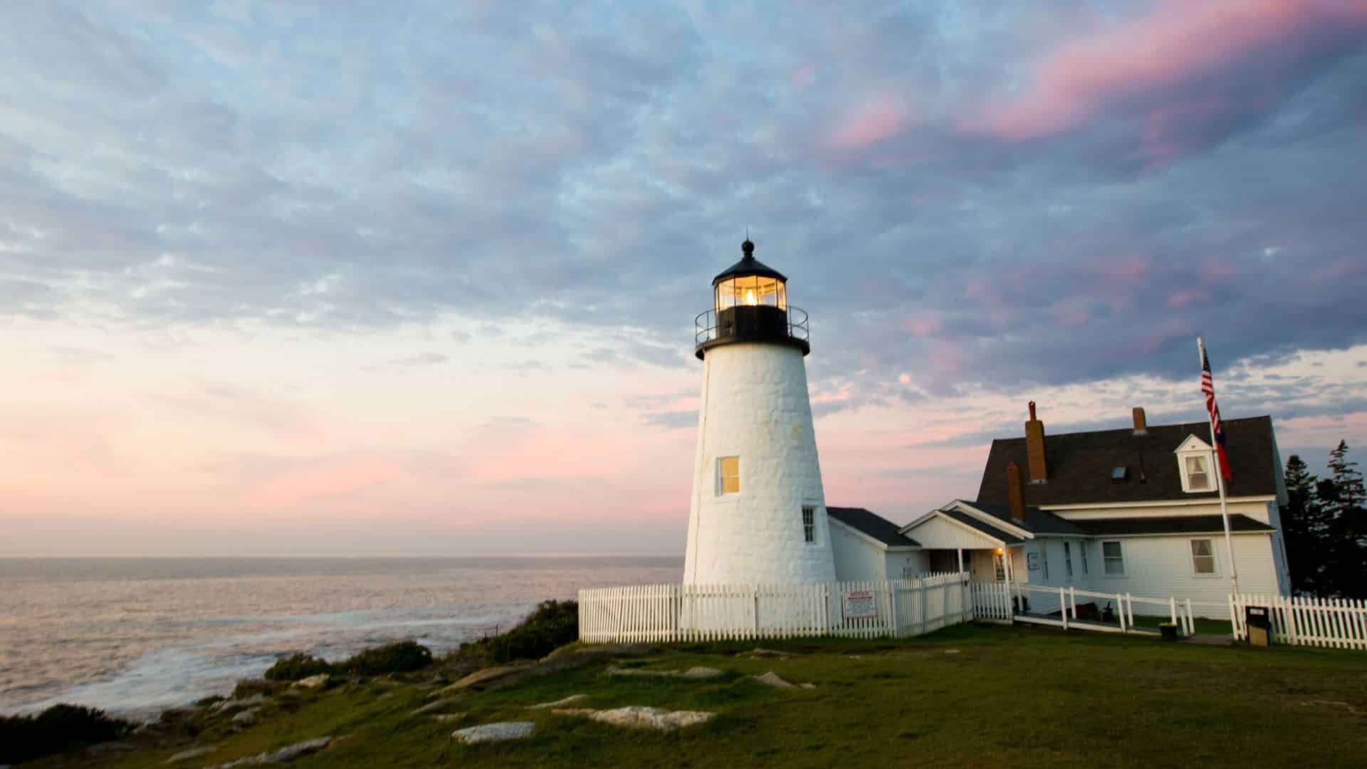 Lighthouse on a hill surrounded by grass with the ocean in the background