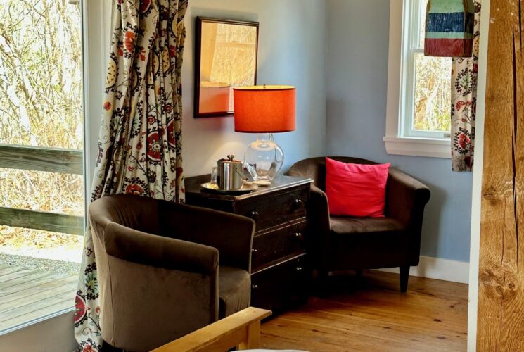 Cozy sitting area with two dark chocolate brown chairs, a small dresser with a lamp, glassware and ice bucket in between French door entry and side window.