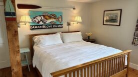 A mission style king bed, wooden floors, lamps on the walls over the bed, a ceiling fan and crisp white linens.