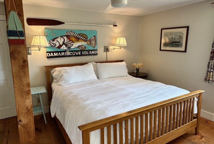 A mission style king bed, wooden floors, lamps on the walls over the bed, a ceiling fan and crisp white linens.