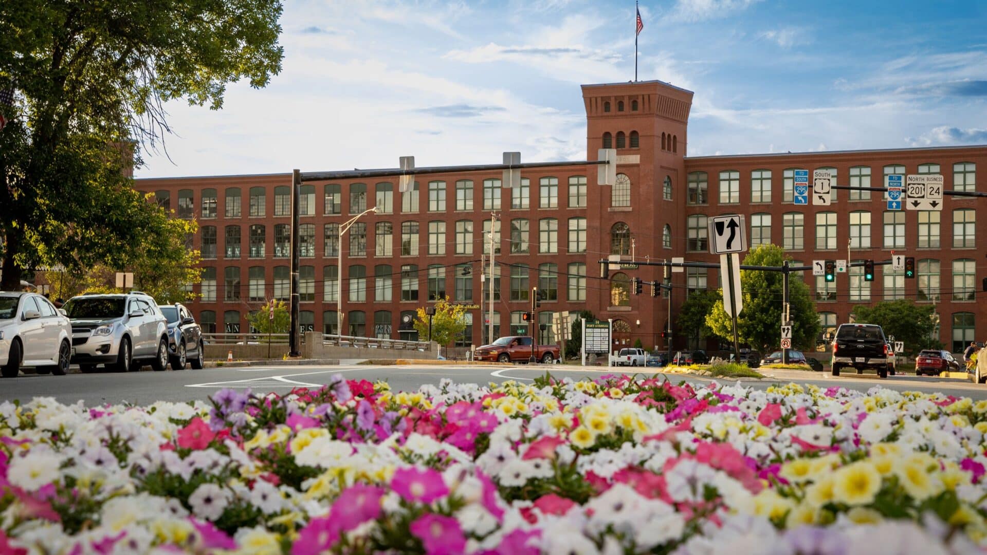 Beautiful petunia flower bed in the foreground in pinks, white, purple and yellow. Fort Andross in the background, a large brick building.