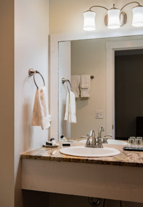 View into the bathroom with crisp, fluffy white towels hanging from the wall over the granite countertop which contains room amenities.