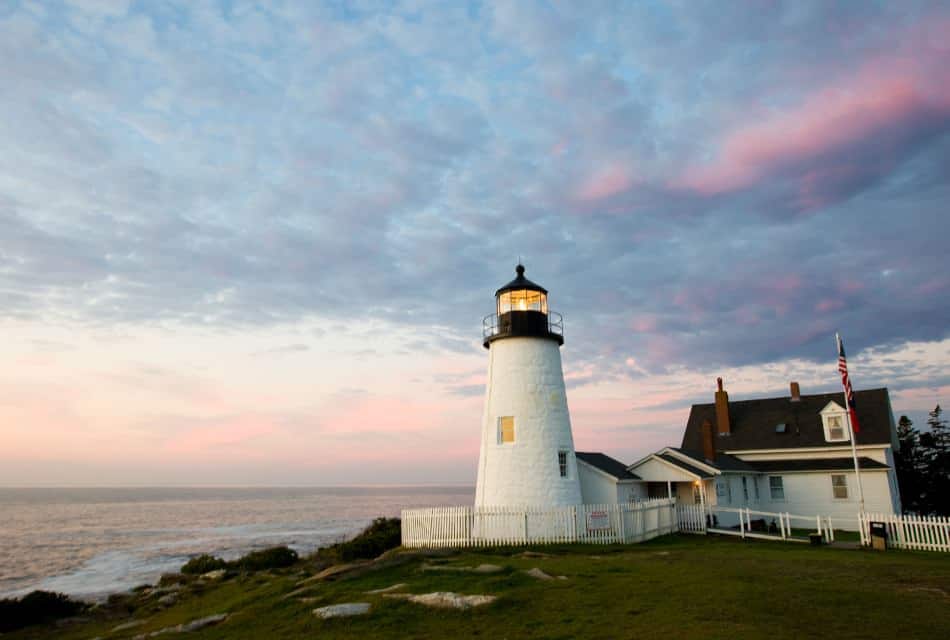 Lighthouse on a hill surrounded by grass with the ocean in the background