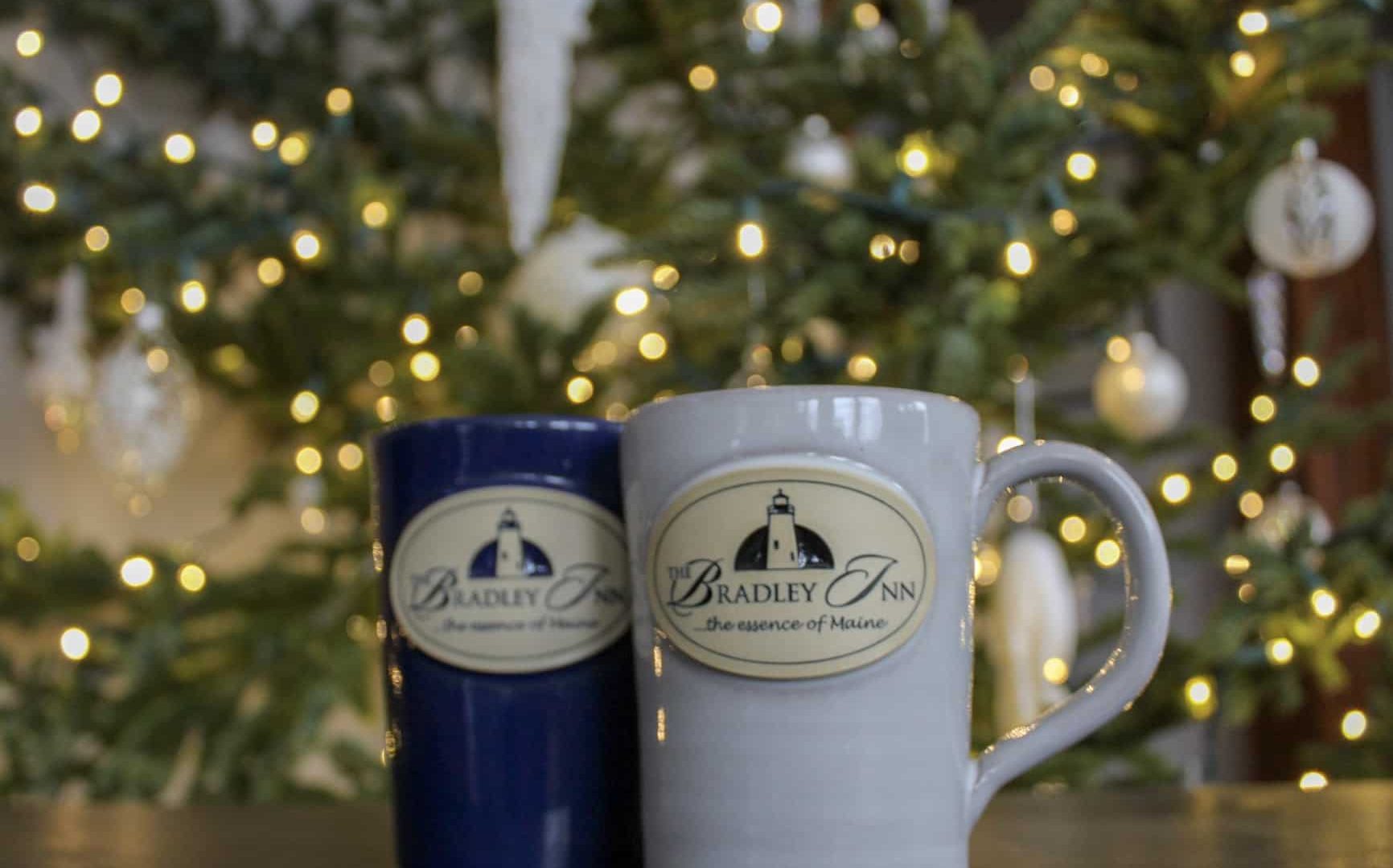 Navy blue and off white bradley inn mugs in front of the christmas tree with white ornaments and tiny white lights.