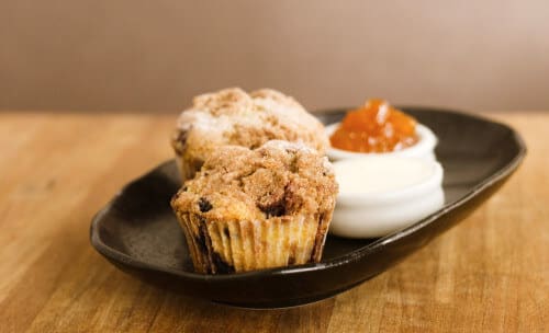 Two muffins on a black plate iwth butter and marmalade. 