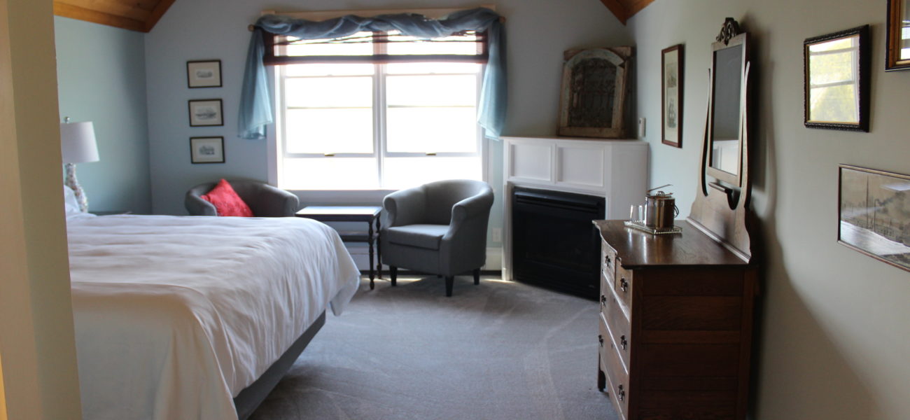 Brown and pink floral wallpaper with bed draped in a pink duvet facing a roaring fireplace.