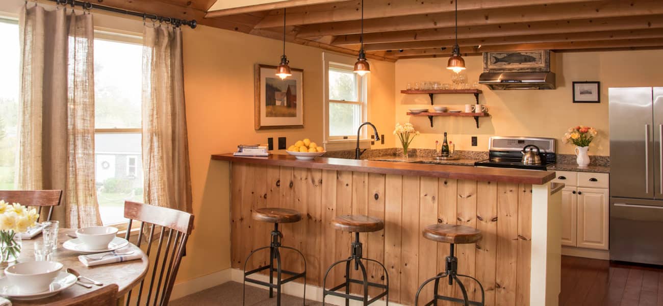 Oak bar with beams overhead and three barstools looking at stainless steel fridge.