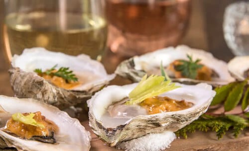 Oysters on the half shell served on a wooden plank with salt, accompanied by wine