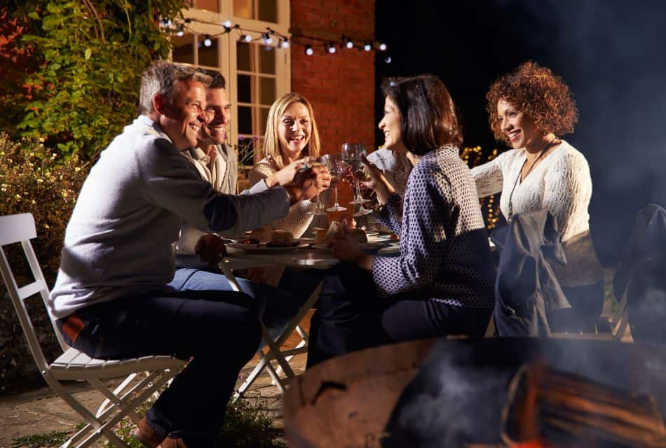 People sitting around a small table on an outside porch toasting and smiling at night