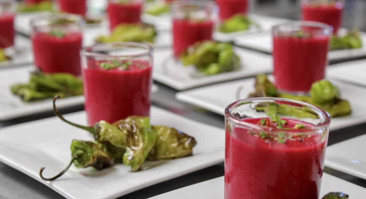 Close up view of many plates with shishito peppers and chilled beet soup