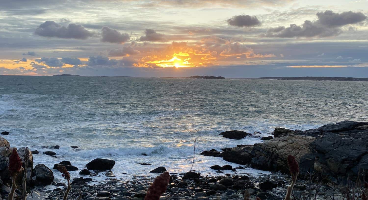 View of the ocean from a rocky beach with an island and setting sun in the background