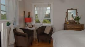 Large bedroom suite with white walls, hardwood flooring, fireplace, white bedding, and sitting area