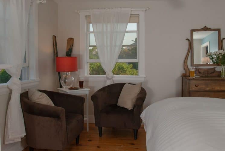 Large bedroom suite with white walls, hardwood flooring, fireplace, white bedding, and sitting area