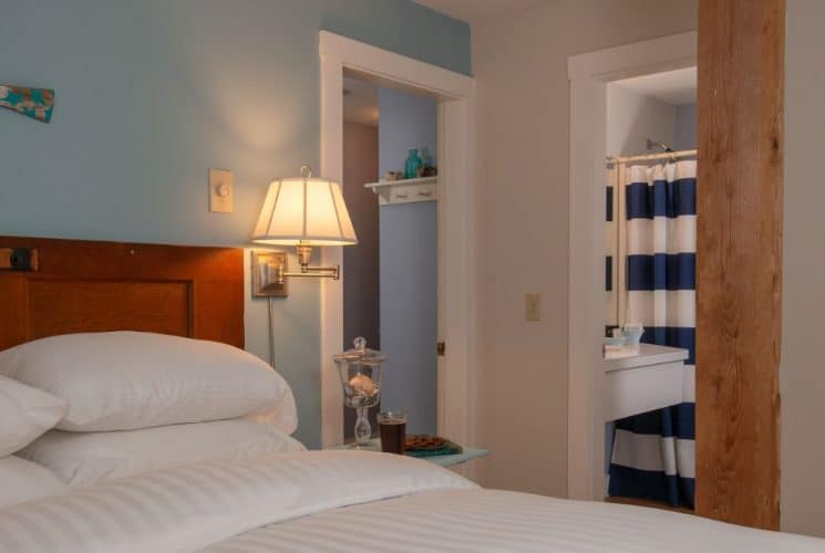 Large bedroom suite with white and blue walls, hardwood flooring, white bedding, and view into bathroom