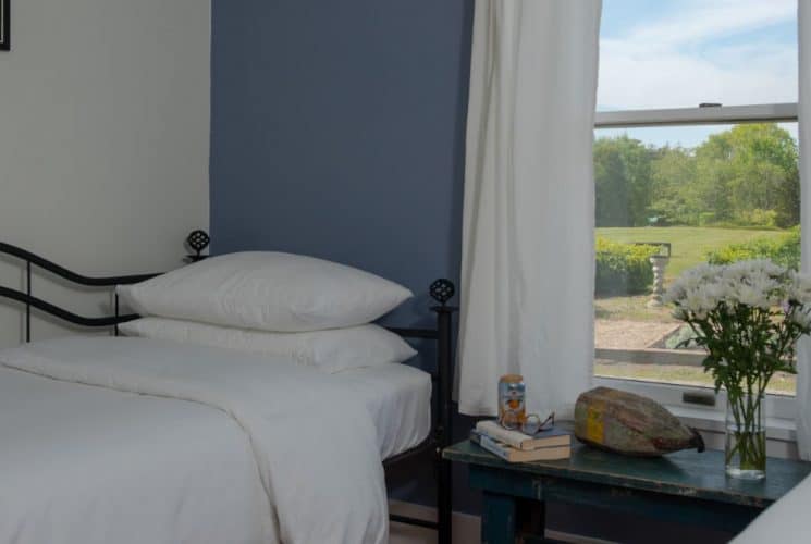 Bedroom suite with white and blue walls, hardwood flooring, white bedding, and view to the outside