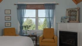 Large bedroom suite with blue walls, white bedding, fireplace, sitting area, and view to the outside