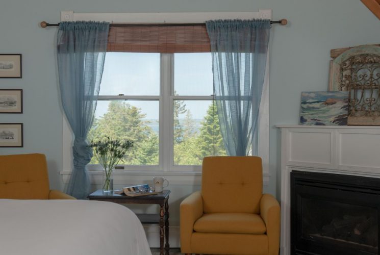 Large bedroom suite with blue walls, white bedding, fireplace, sitting area, and view to the outside