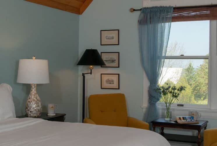 Large bedroom suite with blue walls, wooden headboard, white bedding, sitting area, and view to the outside