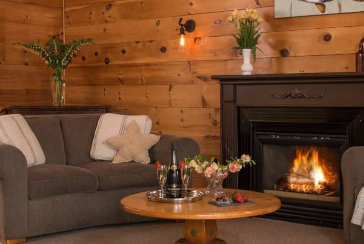 Large gathering room with wood paneling on the walls, upholstered loveseat and chair, fireplace, and wooden coffee table