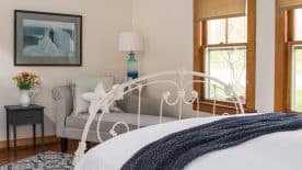 Large bedroom suite with white walls, hardwood flooring, white bedding, chaise, and view to the outside