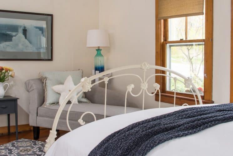 Large bedroom suite with white walls, hardwood flooring, white bedding, chaise, and view to the outside