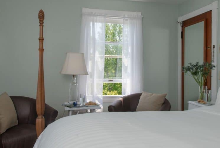 Large bedroom suite with light green walls, wooden four-poster bed, white bedding, sitting area, and view to the outside