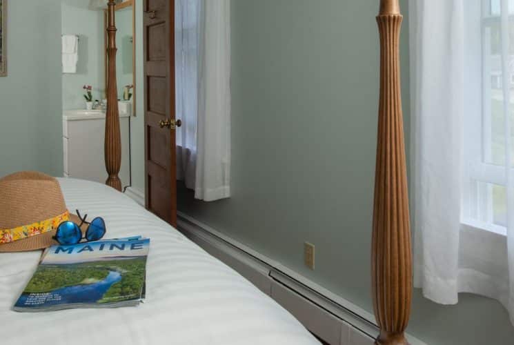 Large bedroom suite with light green walls, wooden four-poster bed, white bedding, and view to the outside