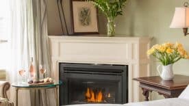 Large bedroom suite with light-colored walls, white bedding, fireplace, sitting area, and view to the outside