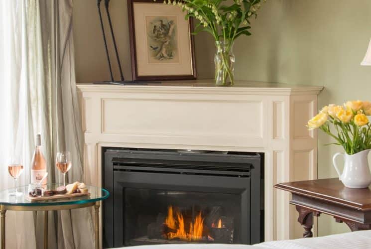 Large bedroom suite with light-colored walls, white bedding, fireplace, sitting area, and view to the outside