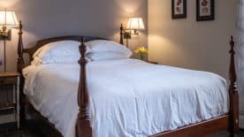 Large bedroom suite with taupe and cream walls, hardwood flooring, dark wooden four-poster bed, white bedding, and view to the outside