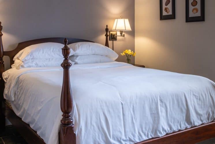 Large bedroom suite with taupe and cream walls, hardwood flooring, dark wooden four-poster bed, white bedding, and view to the outside