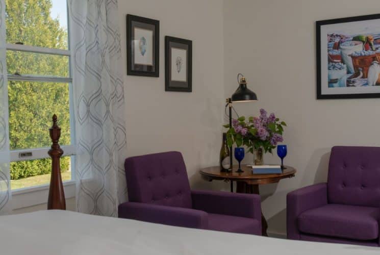 Large bedroom suite with cream walls, hardwood flooring, white bedding, and sitting area