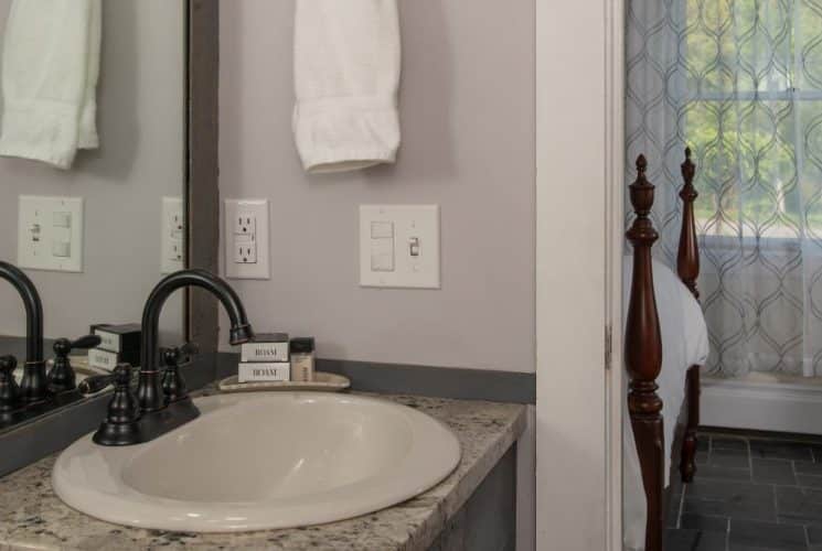 Bathroom with light colored walls, quartz vanity top, white sink, large wooden framed mirror, and view into bedroom