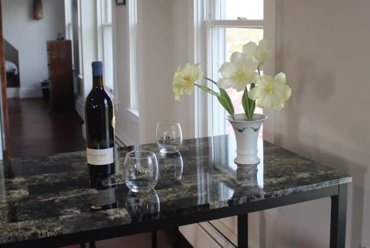 Close up view of small table with quartz top with vase of flowers, wine bottle, and wine glasses