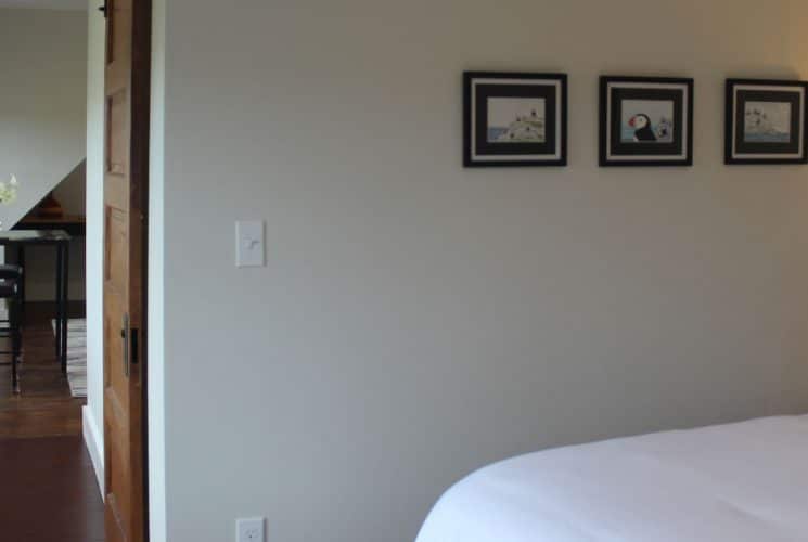 Large bedroom suite with light-colored walls, hardwood flooring, white bedding, and view to adjoining room