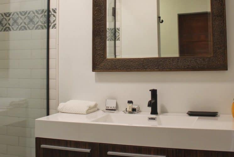 Bathroom with white walls, wooden vanity, white sink, framed mirror, and tiled stand up shower