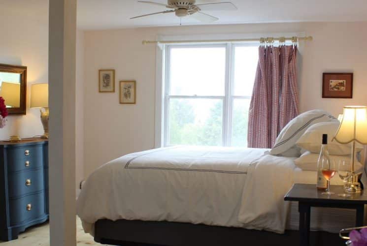 Large bedroom suite with light-colored walls, hardwood flooring, white bedding, and view to the outside