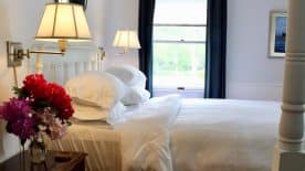 Large bedroom suite with white walls, hardwood flooring, white bedding, and view to the outside