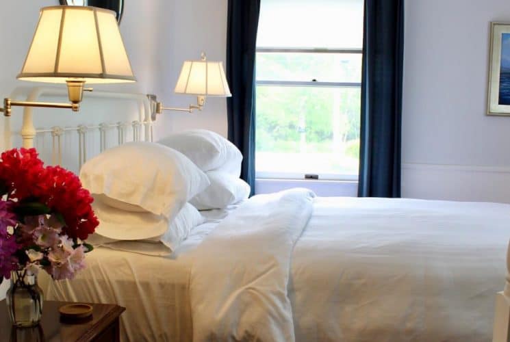 Large bedroom suite with white walls, hardwood flooring, white bedding, and view to the outside