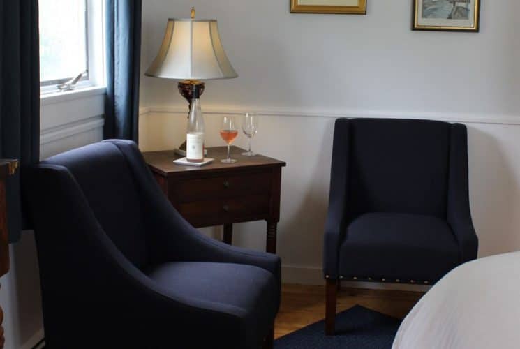 Large bedroom suite with white walls, hardwood flooring, white bedding, and sitting area