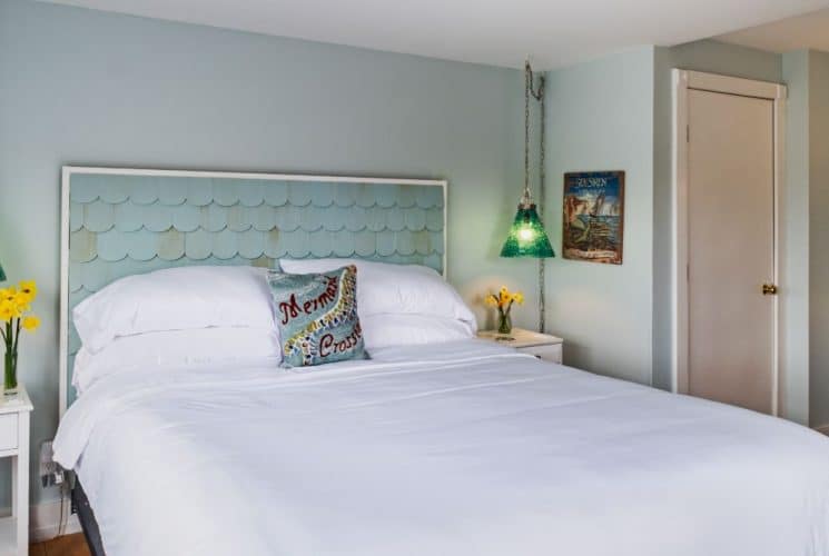 Large bedroom suite with light blue walls, hardwood flooring, white bedding, and green glass lamps hanging from the ceiling