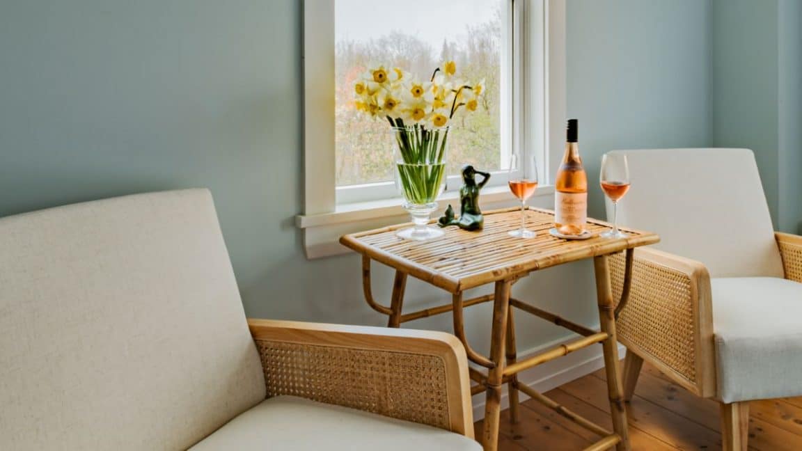 Bedroom sitting area with light wooden chairs each with tan cushions and a wooden table