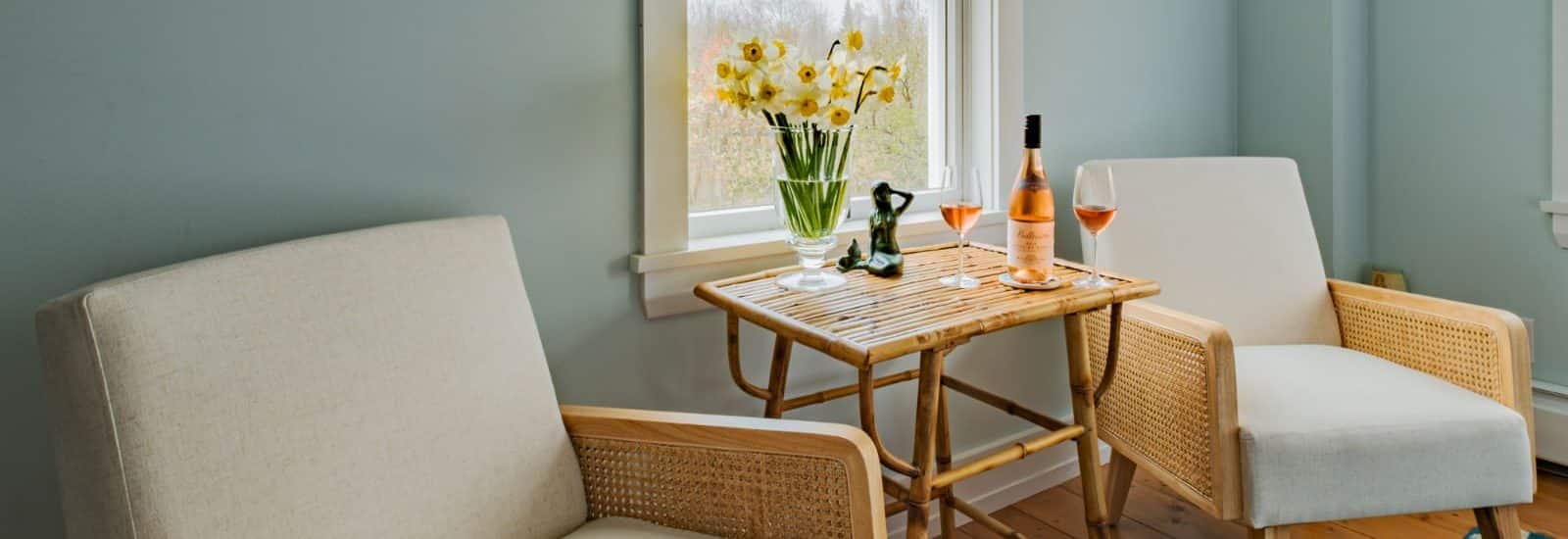 Bedroom sitting area with light wooden chairs each with tan cushions and a wooden table