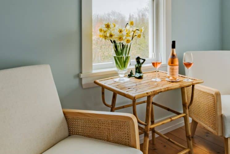 Bedroom sitting area with light wooden chairs each with tan cushions and a wooden table