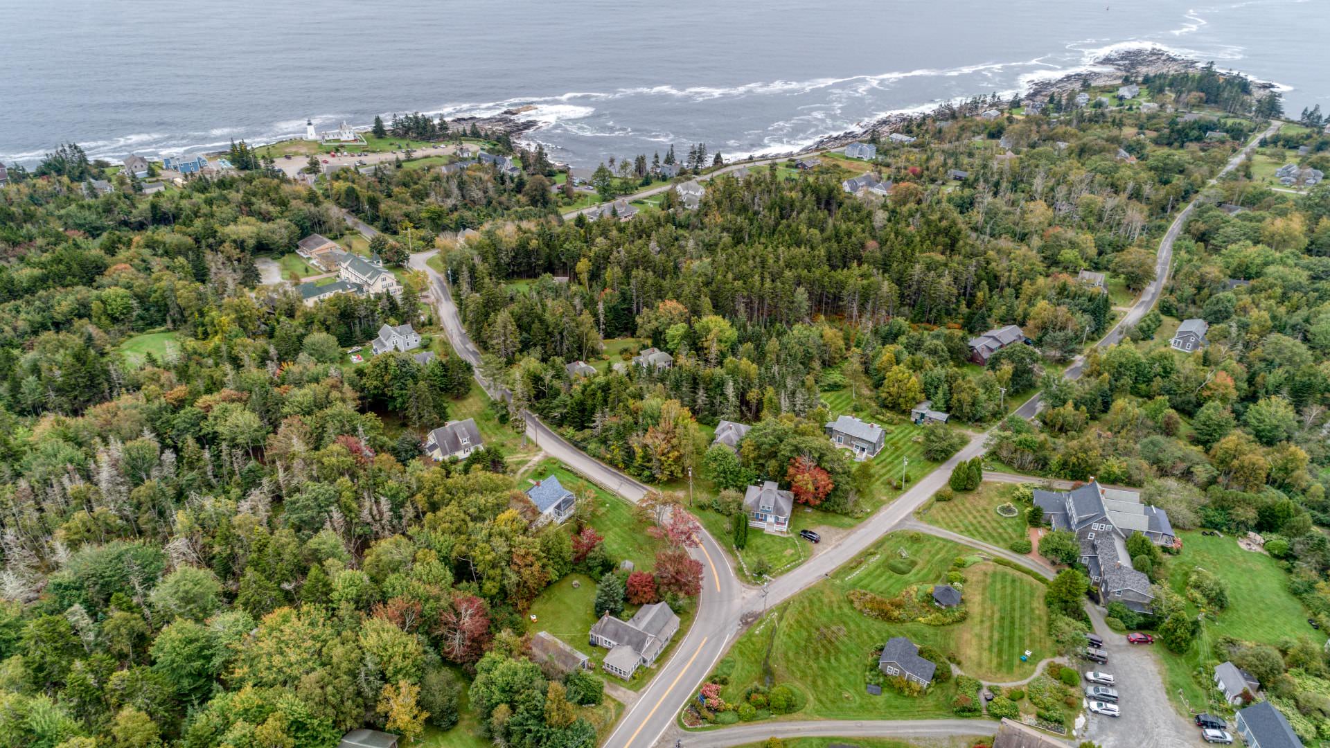 Exterior aerial view of property, other homes, lighthouse, and ocean surrounded by many trees